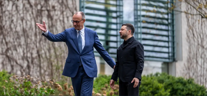 Foto von Merz und Zelinski. Merz zeigt in die Ferne wärend Zelinski sehr verwirrt und niedergeschlagen wirkend zu Merz guckt